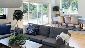 A modern living room with a grey sofa, a coffee table with remote controls, and a dining area with a table and chairs. - Holiday Home in Stjärnhov (Stjarnhov)
