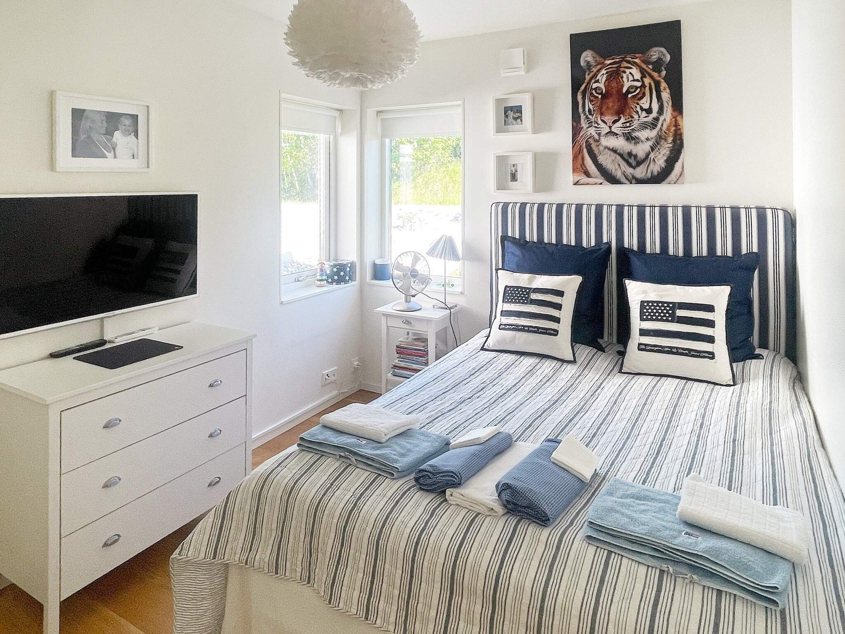 A bedroom with a bed, a TV, a dresser, and a window.