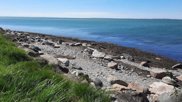 A rocky shoreline with a clear view of the water and distant land.