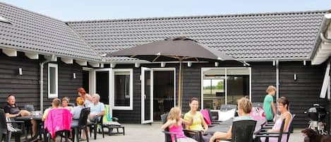 Un espace extérieur aménagé en terrasse avec des tables et des chaises, un coin salon abrité et un chien.