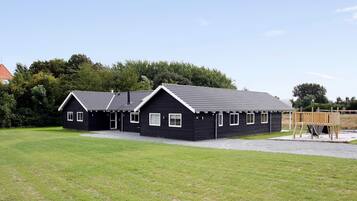 A row of black buildings with white trim, likely a row of cabins or cottages, set in a grassy area with trees in the background.