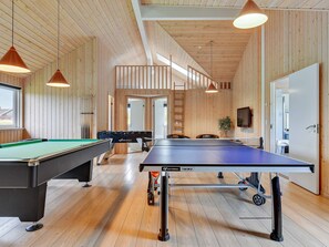 Um quarto com mesa de bilhar, mesa de futebol de mesa e mesa de tênis, com paredes de madeira e teto alto.