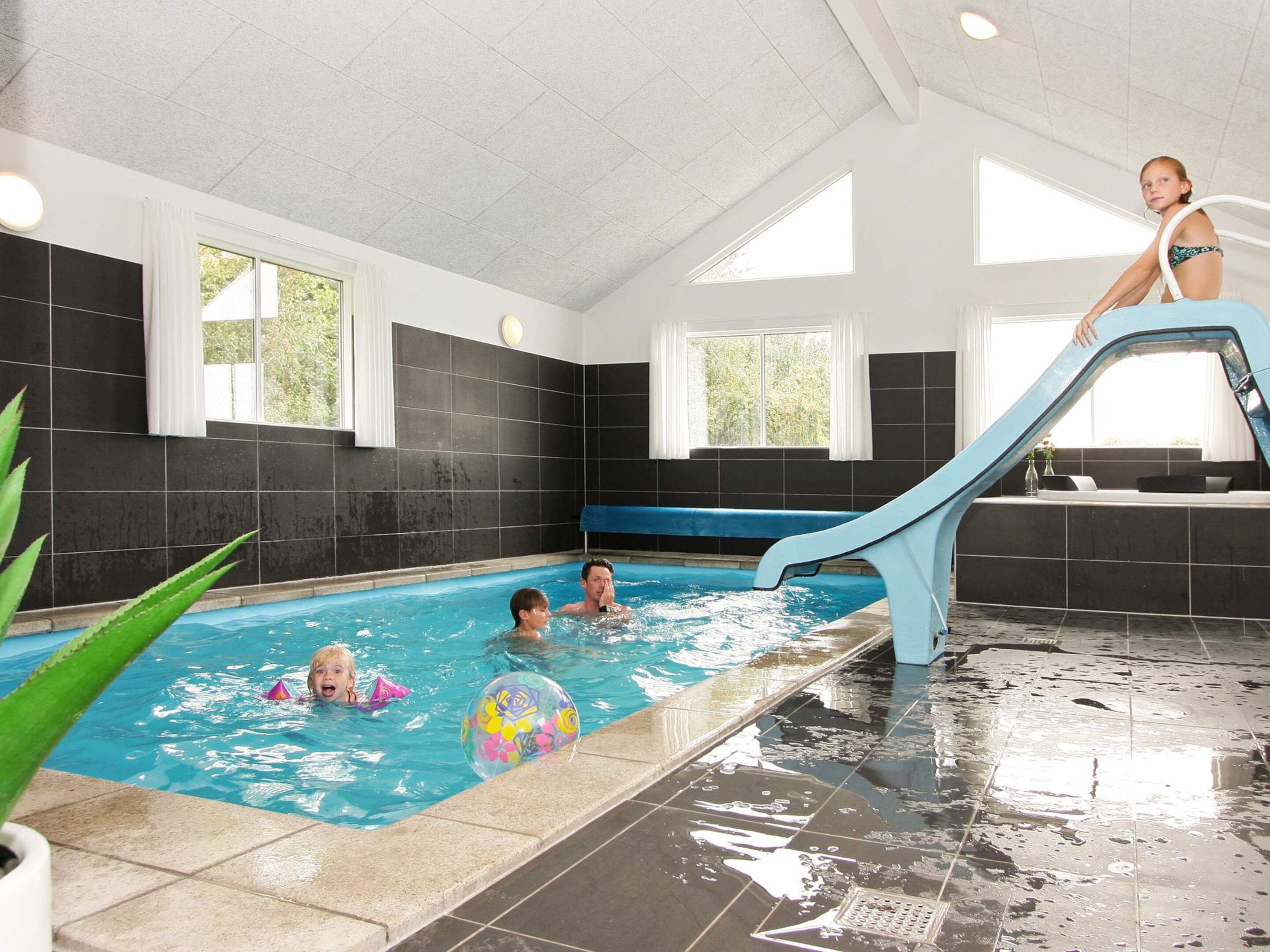 Une piscine intérieure avec un toboggan, des murs carrelés et des fenêtres.