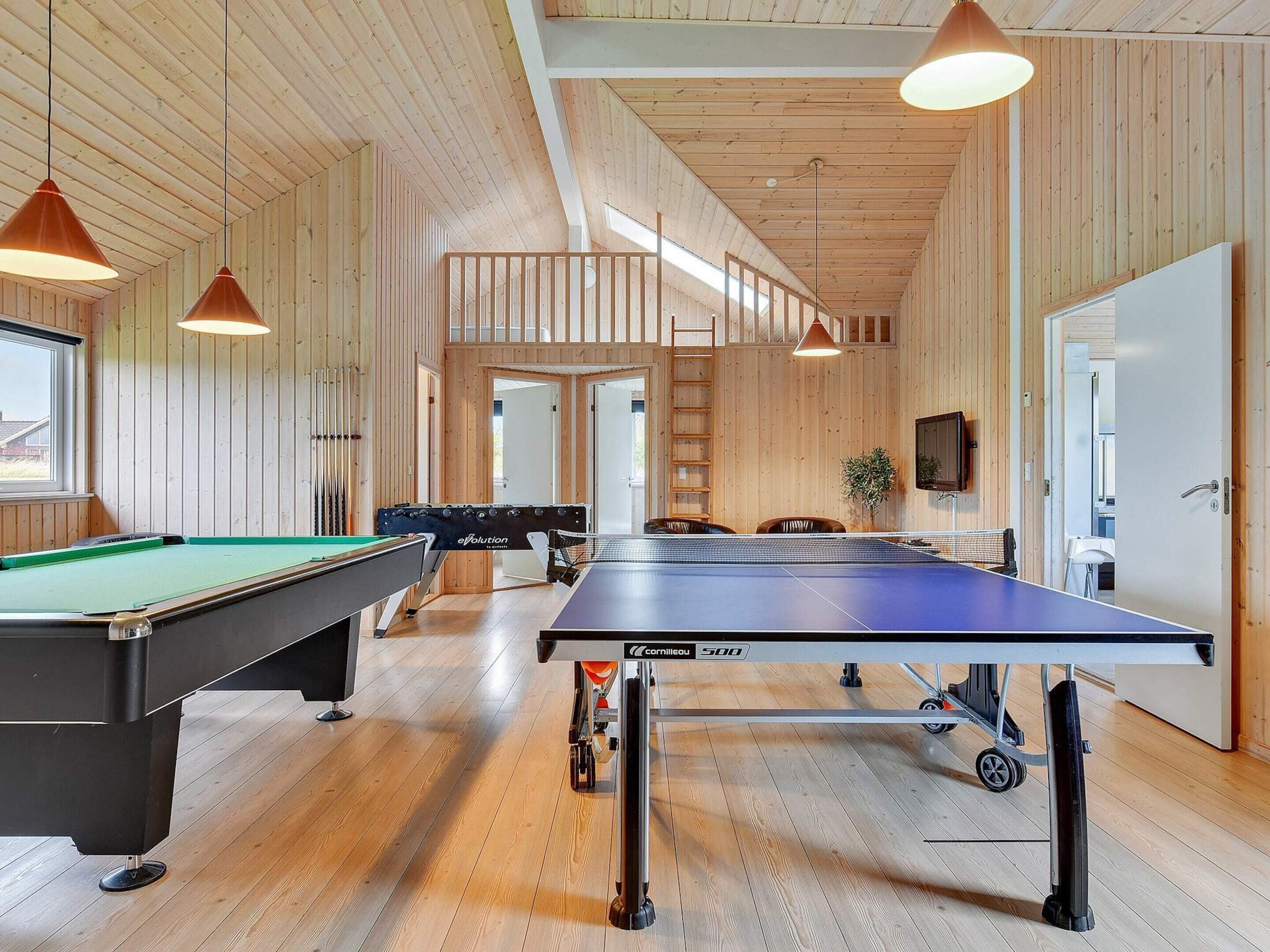 A wooden interior with a pool table, foosball table, and ping pong table.