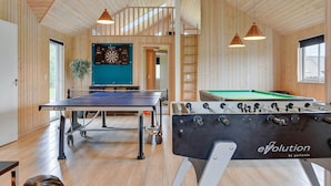 A spacious indoor area with a foosball table, ping pong table, dartboard, and wooden walls.