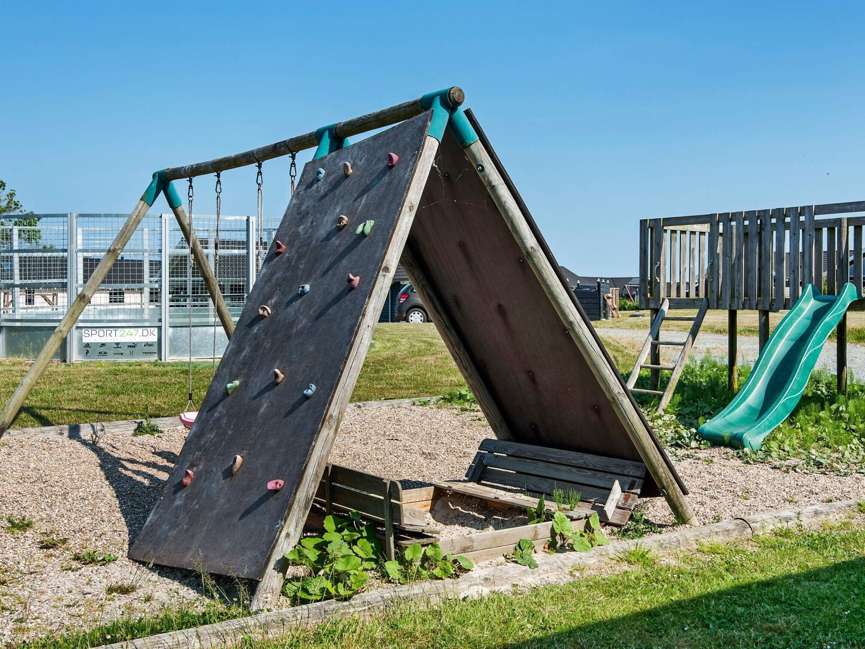 En legeplads med klatrevæg, rutschebane og gyngestativ.