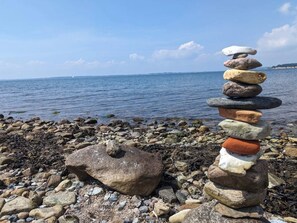 A stack of stones on a pebbly beach with a calm sea and a clear sky in the background. - 5 Star Holiday Home in Sydals (Sydals)