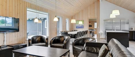 A spacious living area with a high ceiling, wooden panel walls, leather sofas, a dining table, and pendant lighting.