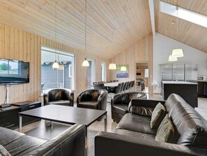 A spacious living area with a high ceiling, wooden walls, a dining table, leather sofas, and pendant lighting. - 5 Star Holiday Home in Sydals (Sydals)