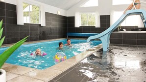 En inomhuspool med en vattenrutschkana, kaklade väggar och fönster.