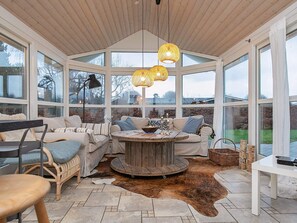 A cozy room with a round wooden table, cushioned seating, and large windows offering a view of the outdoors. - 4 Star Holiday Home in Vaeggerlose (Vaeggerlose)