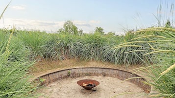 A circular outdoor area with a metal bowl in the center, surrounded by tall grasses and a wooden fence.