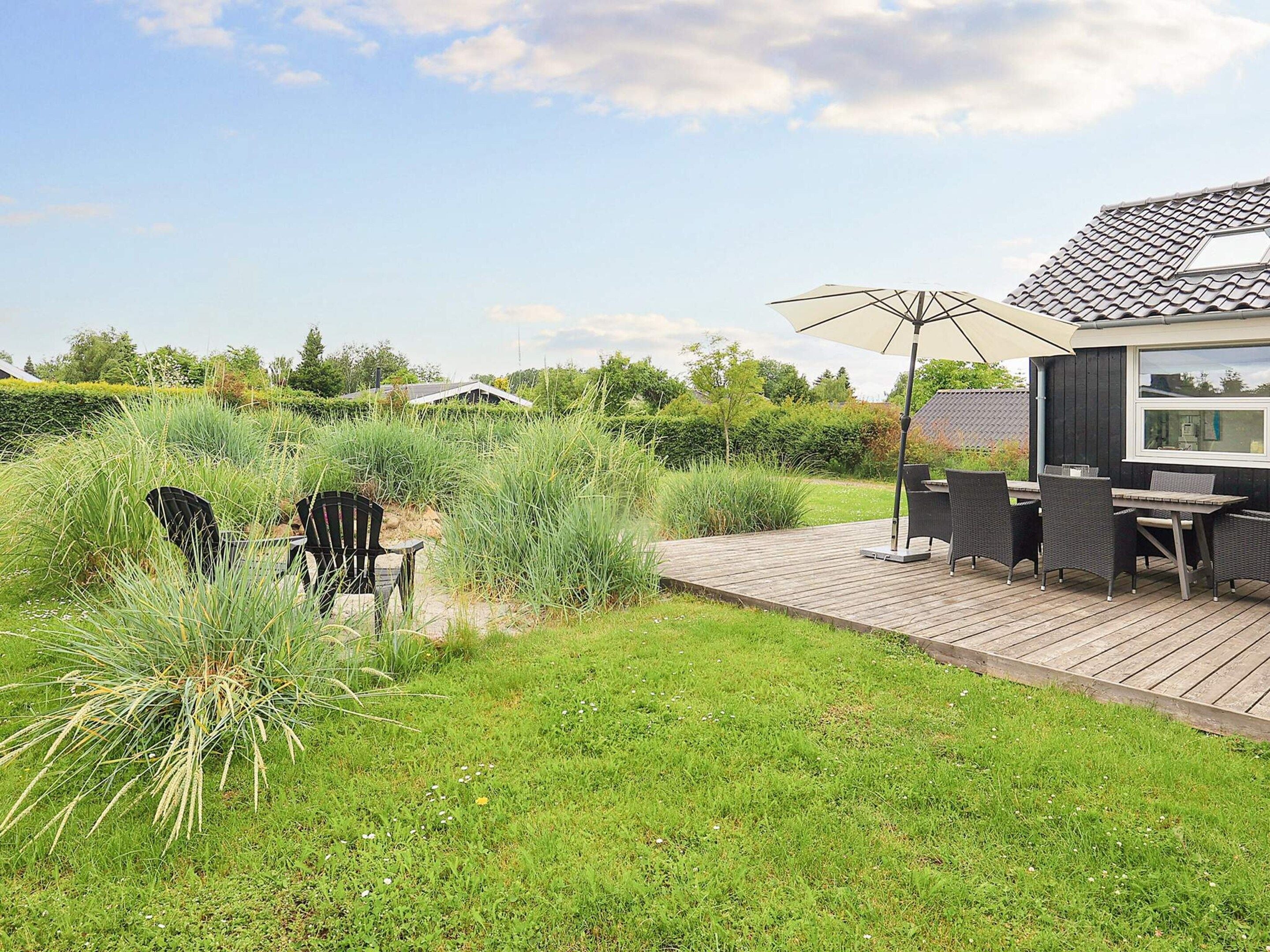 A wooden deck with outdoor furniture, a patio umbrella, and a view of a house with a tiled roof.