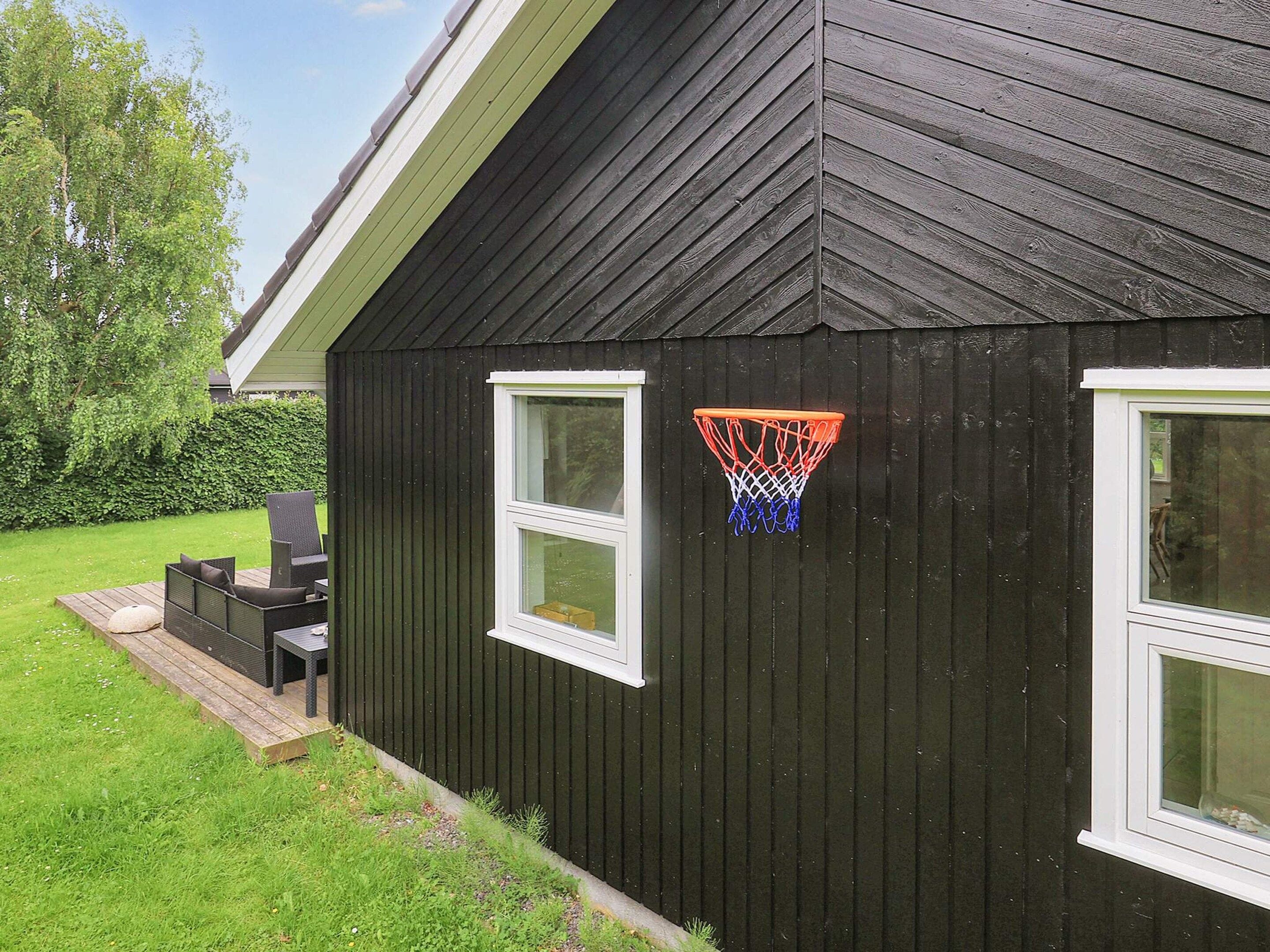 A dark wooden building with two windows and a basketball hoop attached to the wall.
