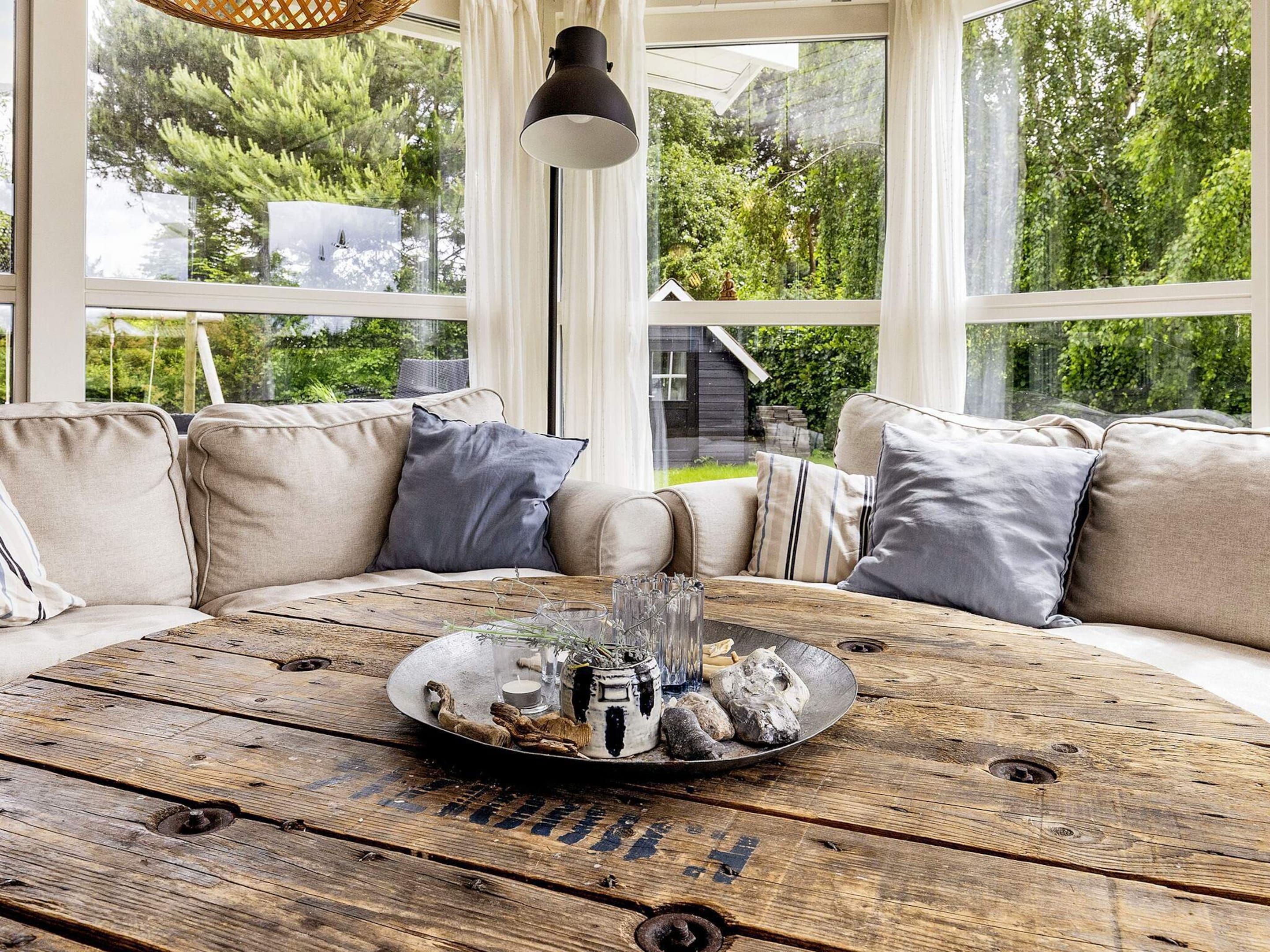 Un rincón acogedor con una mesa de madera, cojines y vistas a la vegetación.