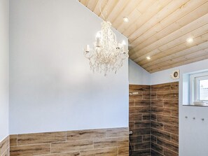 A bathroom with a wooden ceiling, a chandelier, and a shower area with wooden tiles.