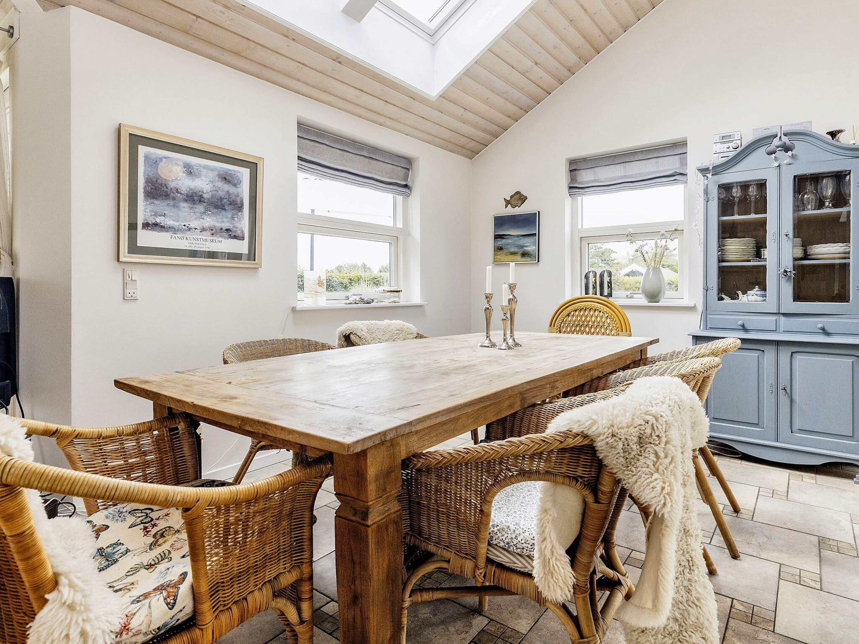 A dining area with a wooden table and wicker chairs, a cabinet with glass doors, and artwork on the walls.