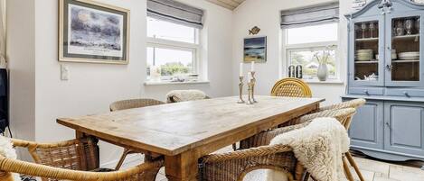 A dining area with a wooden table and wicker chairs, a cabinet with glass doors, and artwork on the walls.