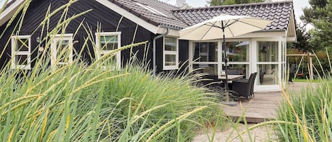Uma casa com fachada escura, telhado em telhas e varanda envidraçada com mobiliário de exterior.