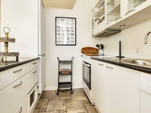 A kitchen with white cabinets, a stainless steel sink, a microwave, and a small wooden shelf.