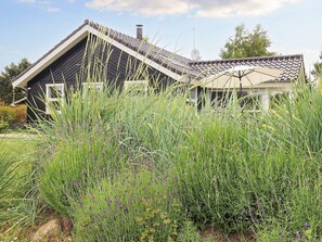 A house with a sloped roof and a chimney, surrounded by tall grasses and lavender.