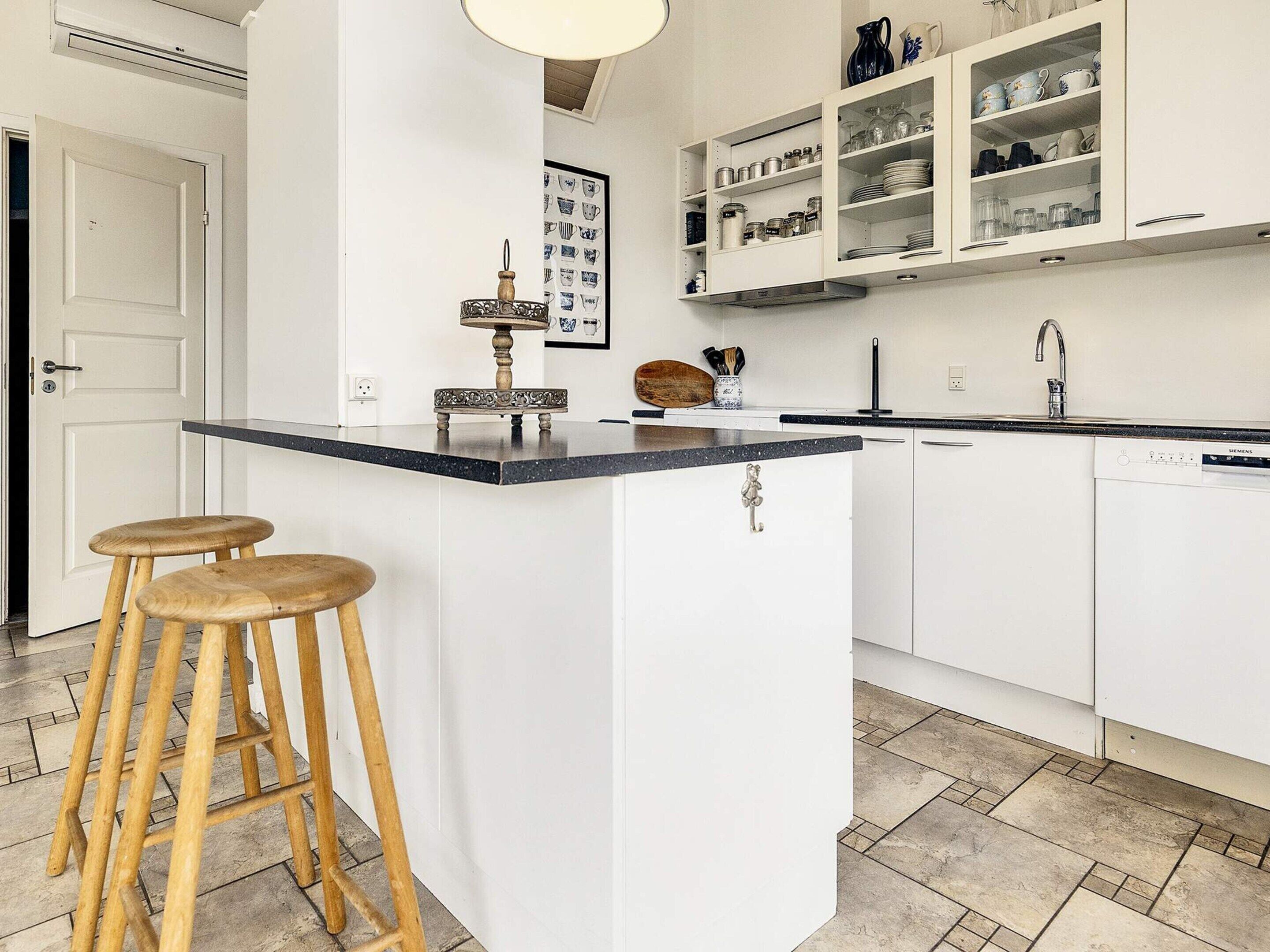 Une cuisine dotée d’un îlot central, de tabourets en bois, de meubles blancs et d’un lave-vaisselle Siemens.