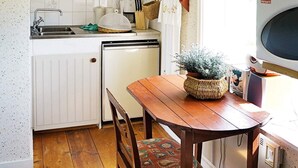 Une cuisine compacte avec des meubles blancs, un évier, un lave-vaisselle et une table à manger en bois, accompagnée de chaises.
