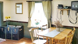 Un coin repas avec une table et des chaises en bois, une valise ancienne et un téléviseur posé sur un meuble en bois.