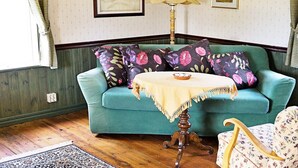 Une pièce avec un canapé de couleur turquoise, une petite table ronde recouverte d’une nappe à franges, un lampadaire et une chaise à motifs floraux.
