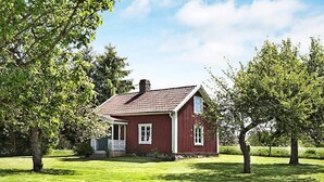 Une maison en bois rouge, avec un toit en pente, une cheminée et une véranda dotée de balustrades blanches.