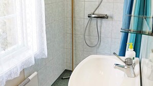A bathroom with a white sink, a shower with a handheld hose, and a window with a sheer curtain.