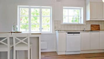 Een keuken met witte kasten, een vaatwasser en een raam met uitzicht op groen.