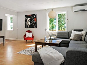 A modern living room with a grey sofa, a red armchair, a coffee table, and a painting on the wall. - Holiday Home in Hova (Hova)