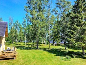 A wooden deck with outdoor furniture, surrounded by a grassy area and trees. - Holiday Home in Hova (Hova)