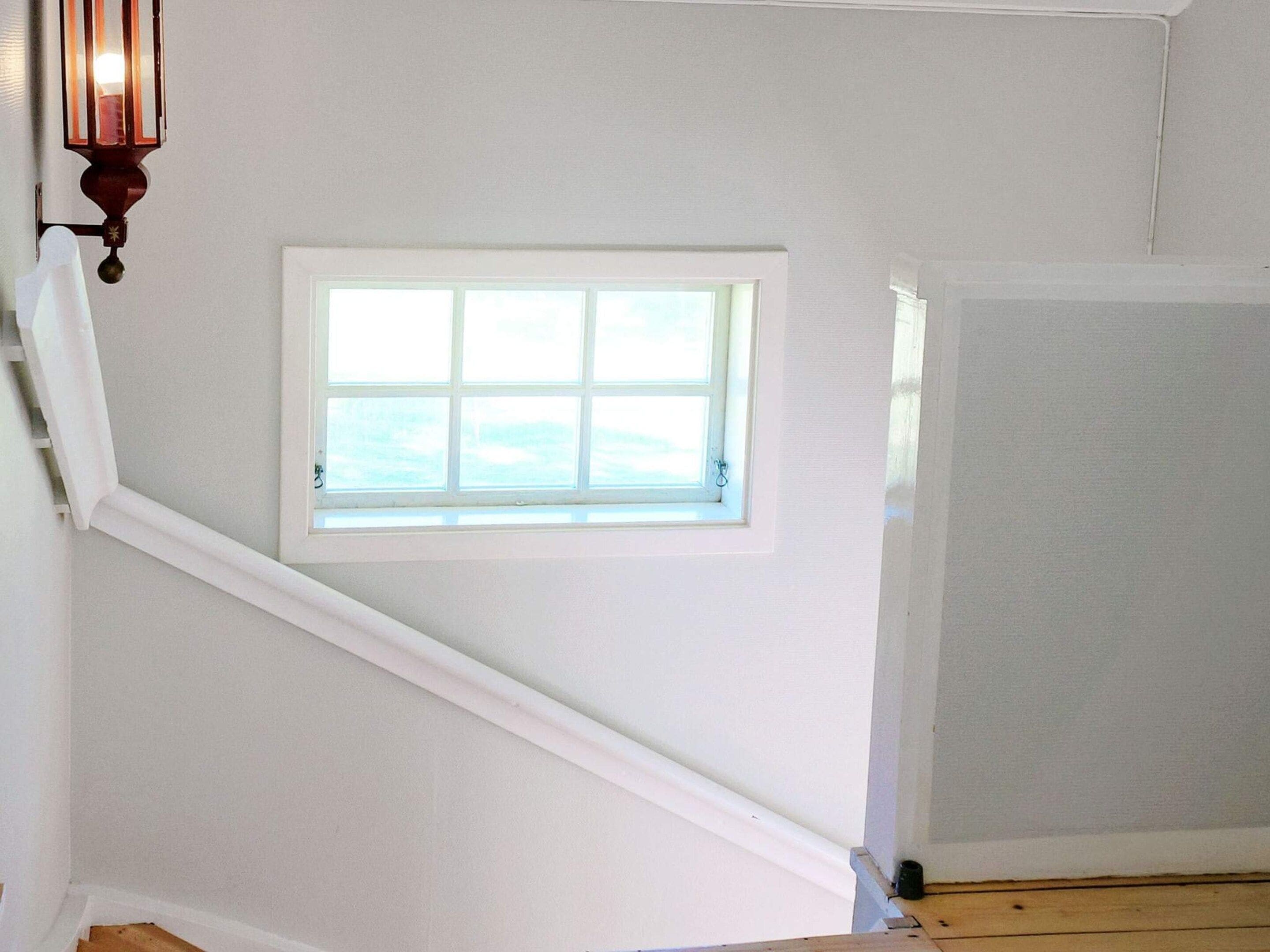 A staircase with a small window, white walls, and a wooden floor.