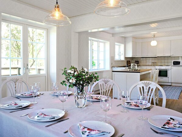 A dining area with a table set for a meal, kitchen in the background, and large windows. - Holiday Home in Hova (Hova)