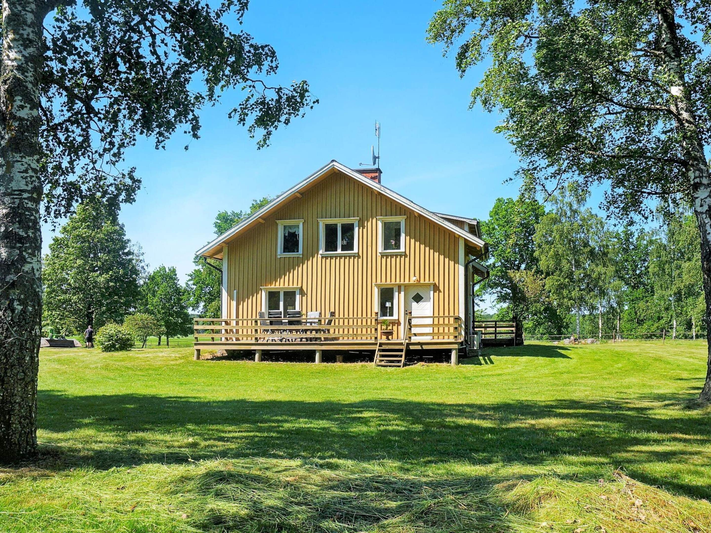 A wooden cabin with a deck, surrounded by trees and grass.