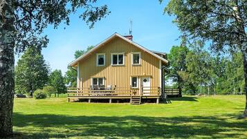 A wooden cabin with a deck, surrounded by trees and grass.