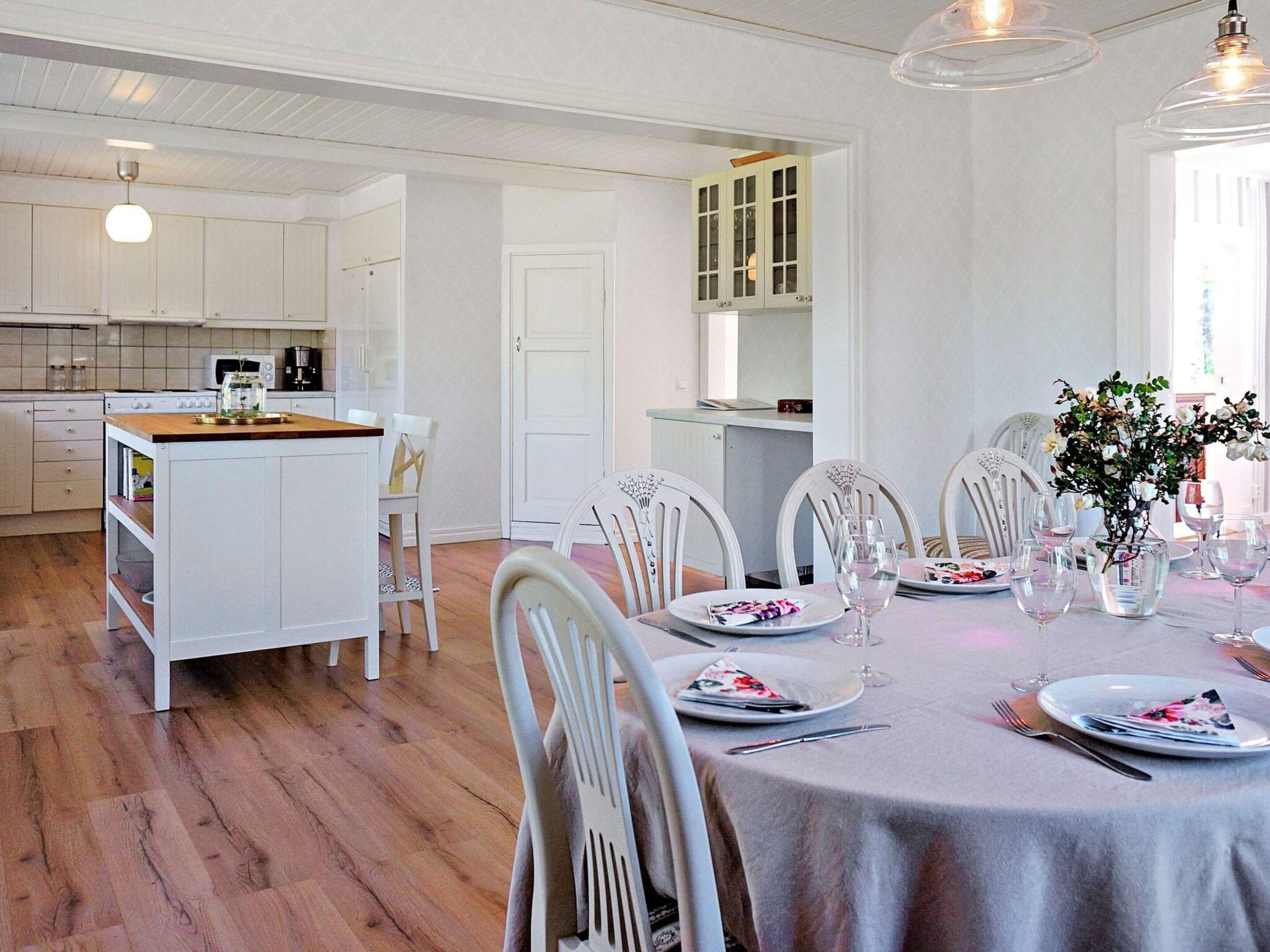 Een moderne keuken met witte kasten, een centraal eiland en een eetgedeelte met witte stoelen en een tafel voor twee personen.