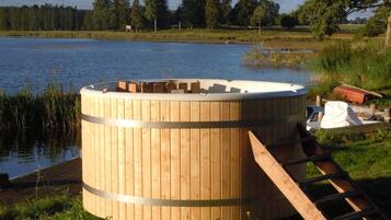 A wooden structure by a lake, possibly a sauna or hot tub, with a ladder leading up.