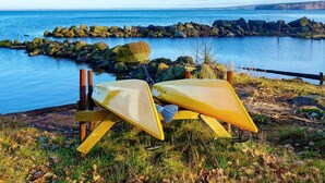 A kayak resting on a wooden stand by a rocky shoreline with a calm body of water and distant land in the background. - Holiday Home in Hova (Hova)