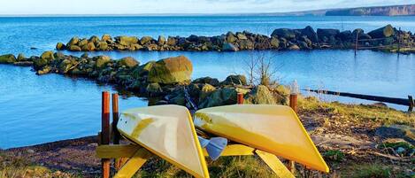 A kayak resting on a wooden stand by a rocky shoreline with a calm body of water and distant land in the background.