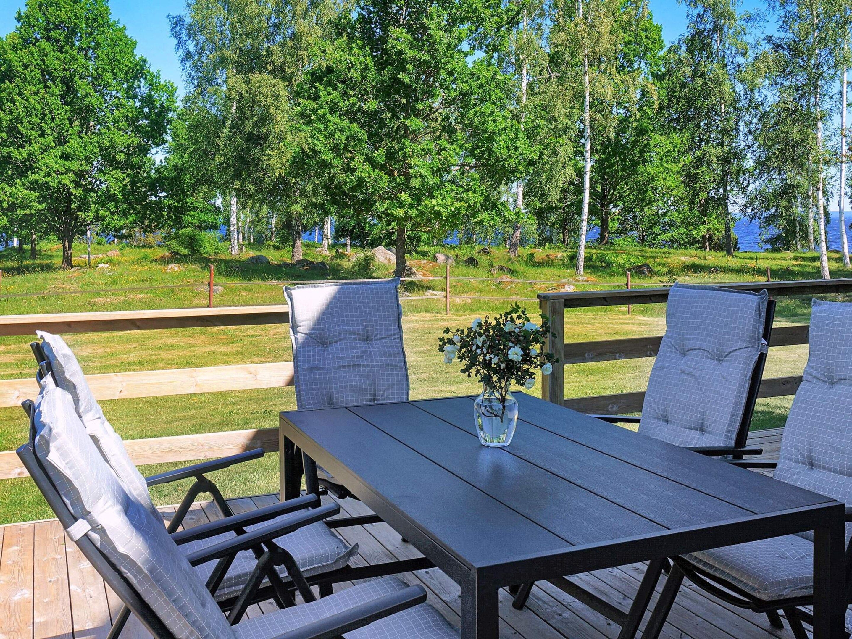 An outdoor dining area with a table and chairs, surrounded by a wooden deck and a view of trees and a body of water.