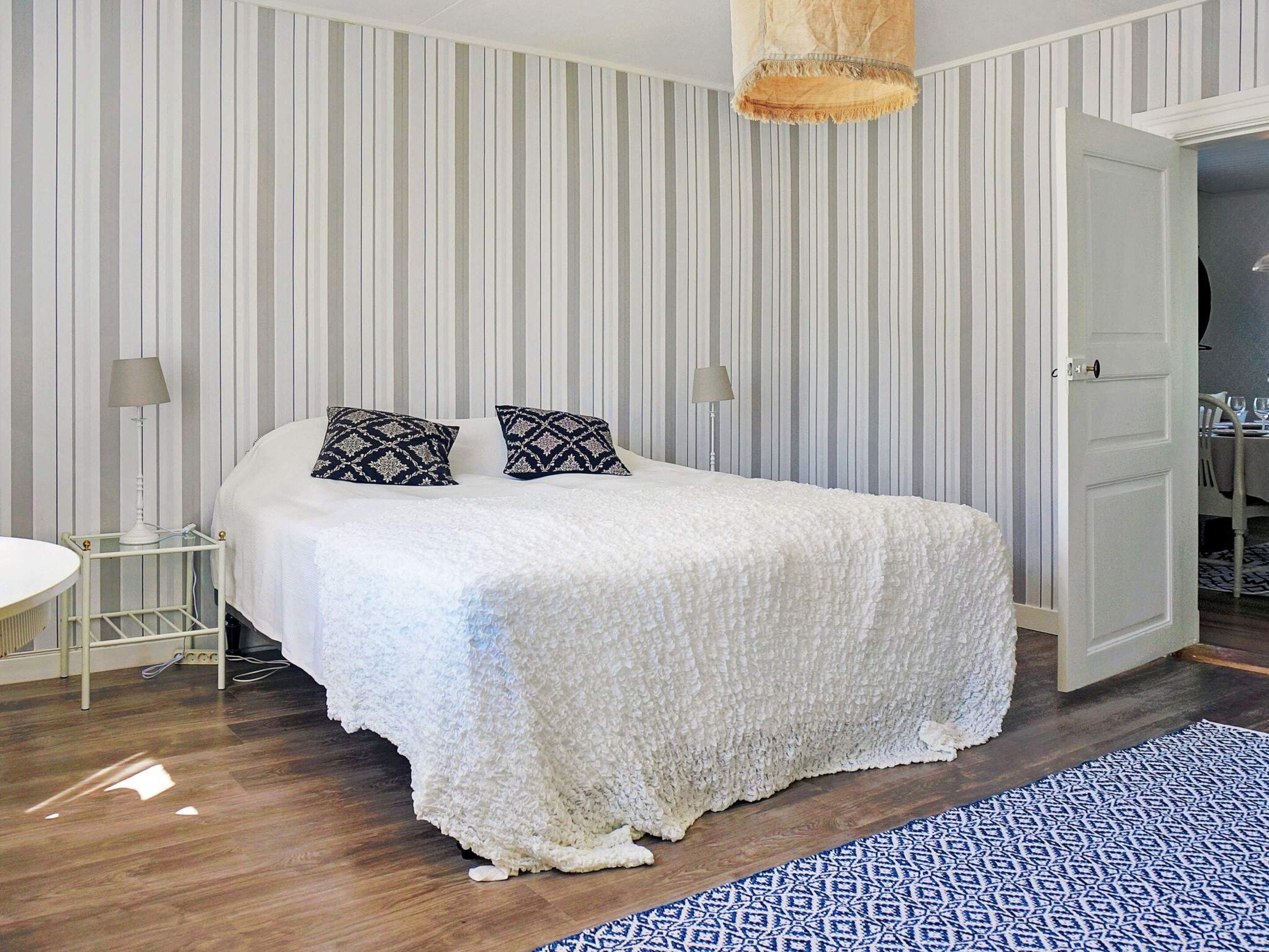 A bedroom with a bed, two bedside lamps, a striped wall, and a patterned rug.