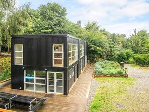Un bâtiment moderne de couleur noire, doté de grandes fenêtres, d’une terrasse en bois et d’un espace jardin.