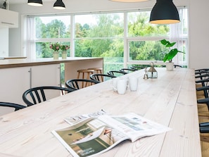 A modern kitchen with a long wooden table, bar stools, and a view of greenery through large windows. - Gorgeous Holiday Home in Ebeltoft with Hot Tub (Ebeltoft)