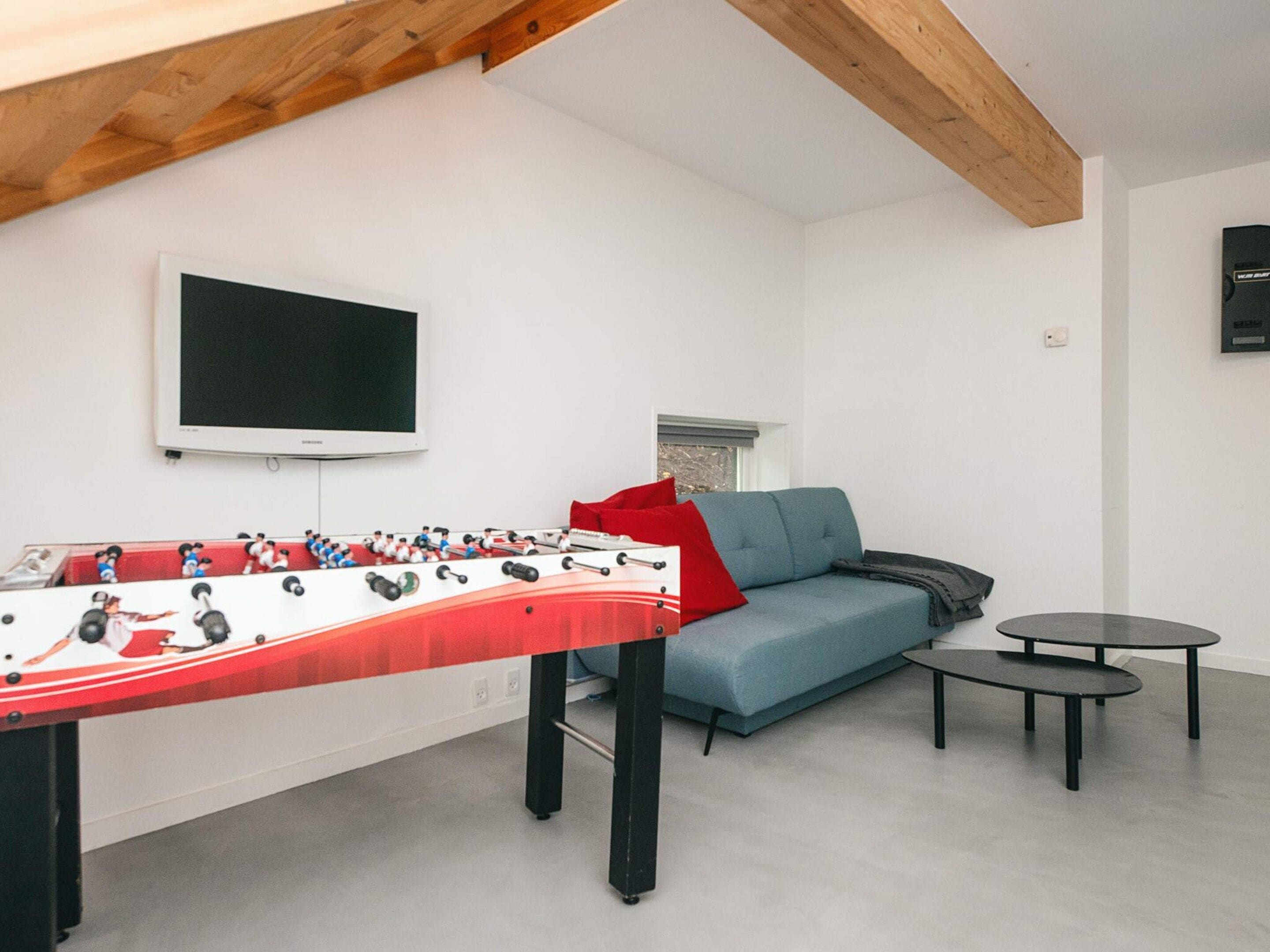 A room with a foosball table, a sofa, a television, and a small table.