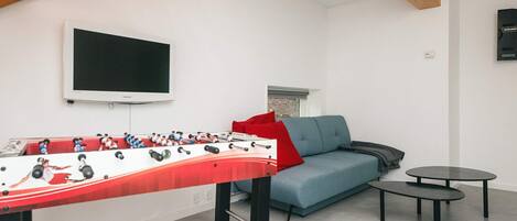 A room with a foosball table, a sofa, a television, and a small table.
