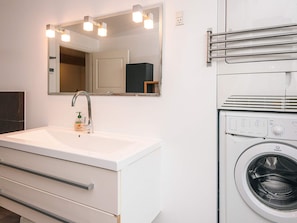 A bathroom with a white sink, a mirror, a hand soap dispenser, a towel rack, and a front-loading washing machine.