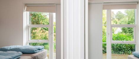 A bedroom with a bed, a window, and a view of greenery outside.